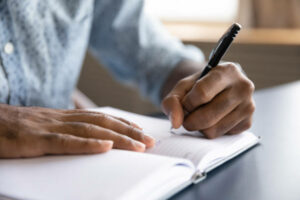 Individual writing in a notebook with a pen