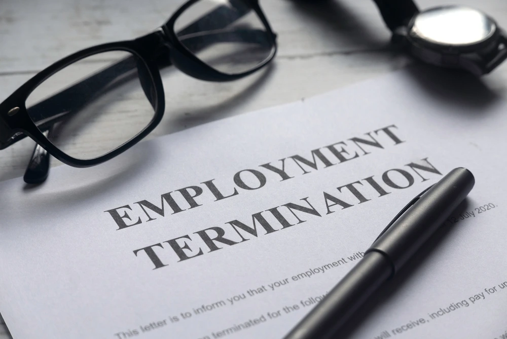 An Overhead Shot Shows A Piece Of Paper Stating &Amp;Quot;Employment Termination&Amp;Quot; Next To A Pen, Glasses, And Watch.